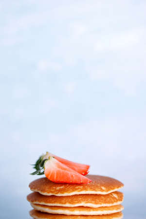 Tasty American pancakes with strawberries on white plate against blue background.の写真素材