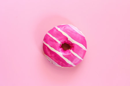Tasty strawberry donut. Homemade circle donut with pink icing and white stripes on the trendy soft pink background situated in the center of image. Donut pastry.の写真素材