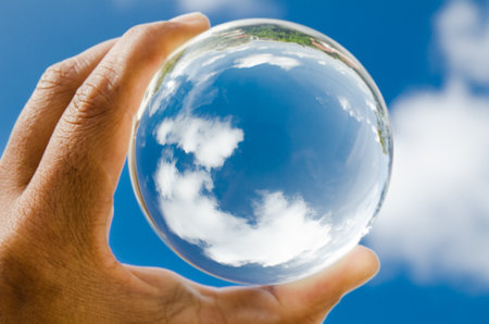 Blue Cloudscape in glass ball holding on male hand.の写真素材