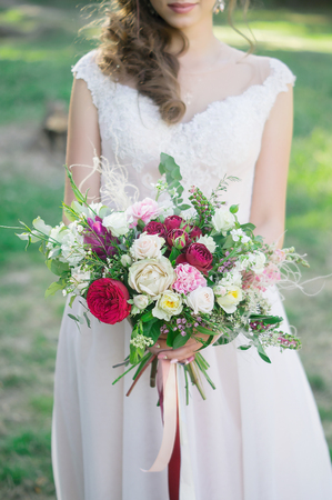 Young bride holds spring wedding bouquet of burgundy roses, pink eustomas, field flowers and green leavesの写真素材
