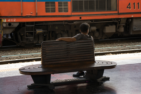 one man is sitting on the wooden bench at the railway stationの写真素材