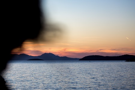 In the calmness of the sailing in Aegean Sea in Greece in the dusk, just on the edge between the golden hour and the blue hour. Seascape with blurred human silhouetteの写真素材