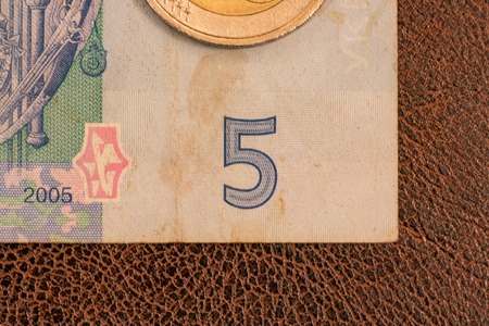 KIEV, UKRAINE - DECEMBER 19, 2014: Ukrainian paper money, hryvnia, lays down on brown imitation leather with patterns. Partial macro photo of the corner of the banknote. Bill of five, two euro coinのeditorial素材