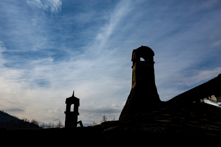 Silhouettes of two retro style chimneys and few leafless trees in Serbia with cloudy blue sky at duskの写真素材