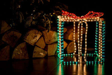 Yellow, green and red lights illuminated present box decoration under Christmas tree with beautifully placed and ordered firewoodの写真素材