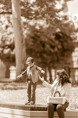 DIMITROVGRAD, BULGARIA - APRIL 30, 2018: Mother stretches her hand to help her son jump from a bench at street concert event dedicated to International World Jazz Dayのeditorial素材