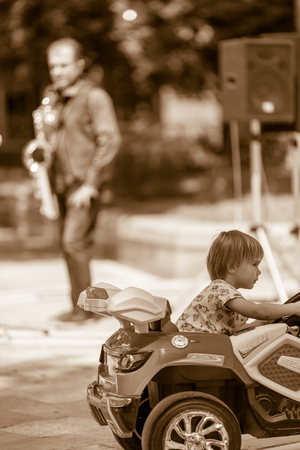 DIMITROVGRAD, BULGARIA - APRIL 30, 2018: Young boy passes in front of the playing musicians driving toy car at street concert event dedicated to International World Jazz Dayのeditorial素材