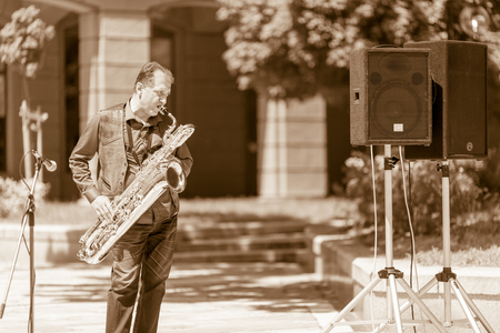 DIMITROVGRAD, BULGARIA - APRIL 30, 2018: Male musician plays on his bass saxophone while looking sideways at street concert event dedicated to International World Jazz Dayのeditorial素材