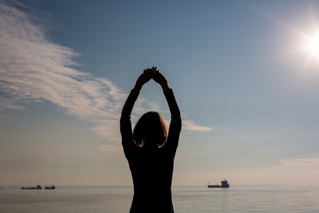 Back view of dancing young beautiful fit woman with short hair in Thessaloniki, Greece. Rear view with blue sea and sky and ship in the backgroundの写真素材