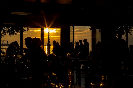 People unrecognizable silhouettes gathering at sunrise in bar sun light on sea water reflection with diffractionsの写真素材