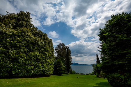Beautiful view of green garden with big trees and birds and picturesque cloudy sky at Isola Bella island in lake Lago di Maggiore. Italy, springtime.の写真素材