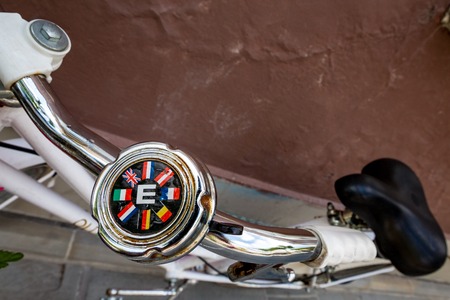 LJUBLJANA, SLOVENIA - JUNE 3, 2014: Metallic bicycle rusty bell with letter E for Europe and flags of eight European countries stands abandoned to rust on white bike steering next to brown city wallのeditorial素材