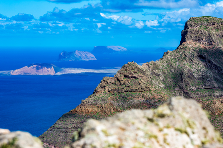 Lanzarote, Canary Islands, Spain, elevated landscape view from mountain peak of blue Atlantic Ocean with expressive bright spring sky with white clouds and three small islands in the backgroundの写真素材