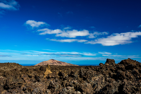 The vast emptiness and loneliness of the Lanzarote black frozen lava volcanic desert and one eroded brown hill in the backgroundの写真素材