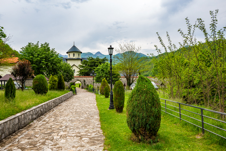 Stone patio in park with green spring grass, bushes and trees leading to the yard of beautiful Orthodox church in Serbiaの写真素材