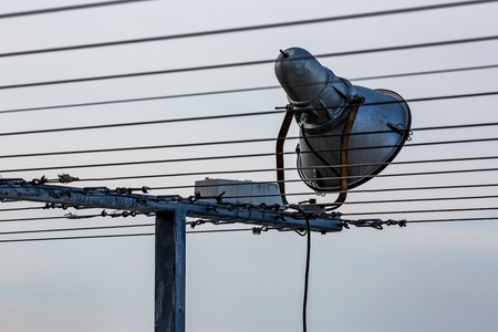 External single cone tin floodlight on metallic steel t-shaped stand with multiple metallic strings, crossing the image, some of them blurred and out of focusの写真素材
