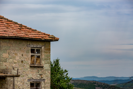 Old abandoned cracked granite stone house with red roof tiles turned into barn stands under the high contrast spring sky of Rhodope Mountains, Bulgaria. Hay stacks could be seen through the windowの写真素材