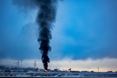 SOFIA, BULGARIA - NOVEMBER 19, 2018: Huge black smoke rises above burning warehouse at the ring road in Bulgarian capital during the first winter day with snow. Industrial plastics fire polluting airのeditorial素材