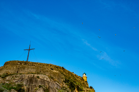 Highest hill in Corfu with Christian Cross on blue sky background. Low angle view of the historic place, now tourist attraction, spring day, Kerkira Island, Greeceの写真素材