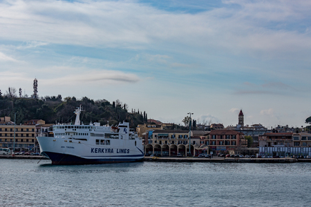 CORFU, GREECE - MARCH 5, 2017: Huge white ferry line waits at ferryboat port of Corfu, Kerkira island in beautiful clouds sky in calm spring day. Town, church tower and boardwalk in backgroundのeditorial素材