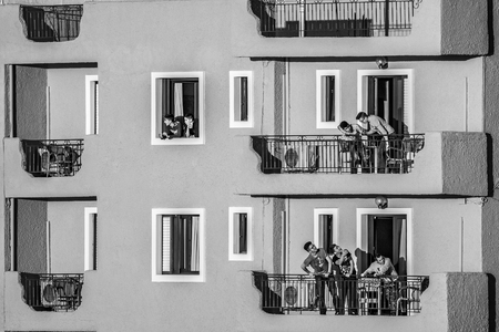 IGOUMENITSA, GREECE - MARCH 2, 2017: Group of young men speak to each other from the balconies and windows of a hotel on the boardwalk of the town as seen from the port, black and white photographのeditorial素材
