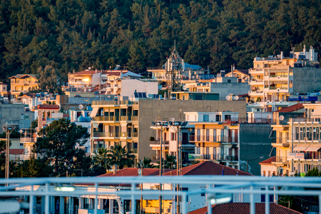 IGOUMENITSA, GREECE - MARCH 2, 2017: Last rays of light from setting Sun fall upon Greek town of Igoumenitsa, residential buildings, cell tower and pine tree forest in the frame as seen from the portのeditorial素材