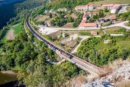 Long empty freight train with many goods wagons passes near the psychiatric hospital near Karlukovo, Northern Bulgaria in sunny autumn day, landscape from high aboveの写真素材