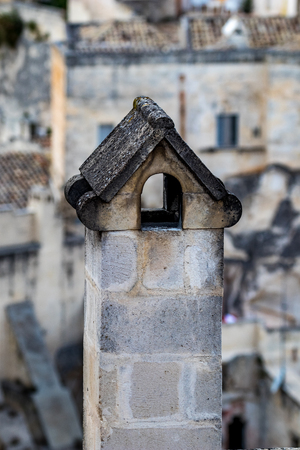 Summer day high-angle scenery street view of a smoked chimney over the amazing ancient town of the Sassi with blurred background of pattern of buildings in Matera, Basilicata, Italyの写真素材