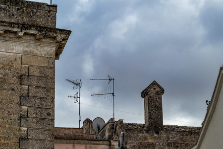 Summer day high-angle scenery street view of a roof with smoked chimney and two antennas in amazing ancient town of the Sassi with blurred cloudy sky background in Matera, Basilicata, Italyの写真素材