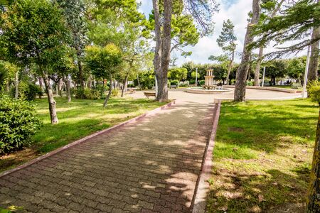 Alley in the tree shadows with round square and fountain in public park, Noci. Puglia. Italy, sunny and warm summer dayの写真素材