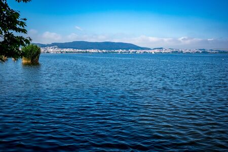 Calm and tranquil water of lake Pamvotida near the Greek town of Ioannina, early spring morning with fog, selective focus, landscape view from Ioannina Island with the town in the background far awayの写真素材