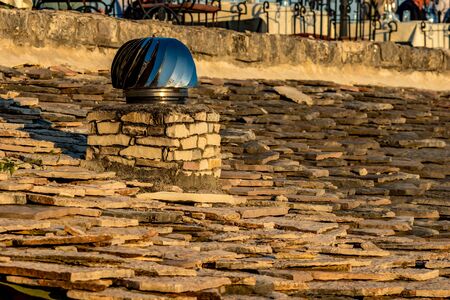 Rotating metallic with blue shades spinner chimney vent on stone tiled roof, Saranda, Albania, photo taken in the golden hour of spring eveningの写真素材