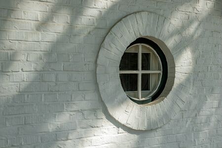 Small round window with bars on white wall. Street view of beautiful historic city center...
