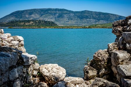 Sunny spring day view of salt lagoon lake, valley and mountain in the national park of Butrint in Albania, Europe. Fortress stone ruined wall in the foreground.の写真素材