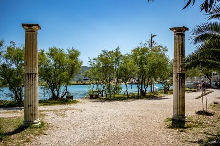 BUTRINT, ALBANIA - JUNE 7, 2019: Two Roman entrance columns. Tourists look at park map. Beautiful warm spring day at archeological site Albanian UNESCO heritage. Photography with fresh green floraのeditorial素材
