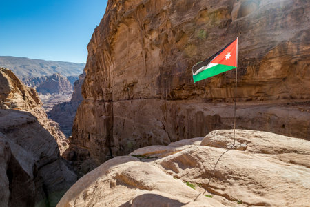 Cliffs and Jordanian flag under the sunlight. I enjoyed the amazing views from the scenery Monastery Route, beautiful sunny day at Petra complex and tourist attraction, Hashemite Kingdom of Jordanの写真素材