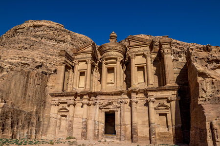 Sunny cloudless day rocky foreground view of the stunning Ad-Deir in the ancient city of Petra, Jordan. Ad-Deir or The Monastery. Petra complex and tourist attraction, Hashemite Kingdom of Jordanの写真素材
