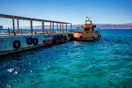 Aqaba, Jordan - February 2, 2020: Big tourist boat with glass bottom, painted in orange waits at the port for tourists to take a trip at Red Sea. Cloudless clear sky winter day. Horizontal frameのeditorial素材