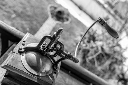 Vintage manual coffee grinder or mill, monochromatic metal high-contrast black and white picture. Partial diagonal composition view from above. Shallow selective focus on transmission elementsの写真素材