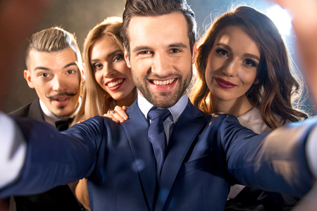 Happy stylish young friends taking selfie and smiling at camera while celebratingの写真素材