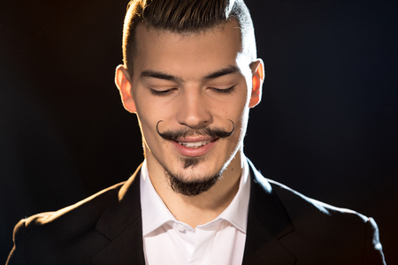Close-up portrait of handsome bearded man in suit smiling on blackの写真素材