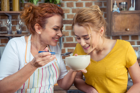 Smiling mother and daughter looking in bowl while cooking together in kitchenの写真素材