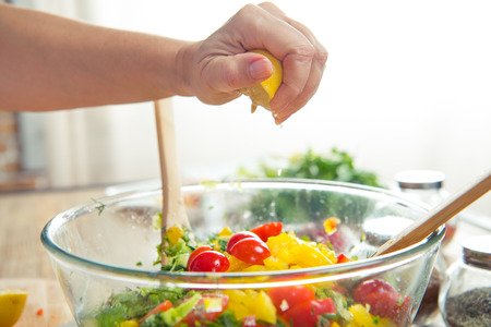Close-up partial view of woman squeezing lemon in bowl with vegetable saladの写真素材
