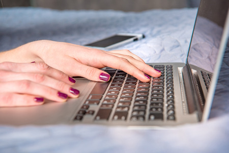 Close-up partial view of young woman using laptop on bedの写真素材