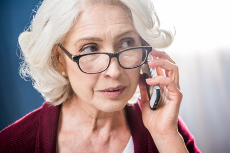 Attractive senior woman in eyeglasses talking on smartphone