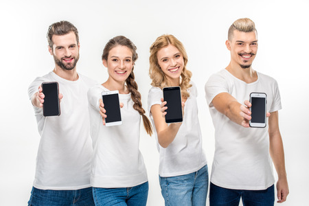Smiling young people showing smartphones with blank screens and looking at camera