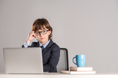 Schoolchild in business suit sitting on desk and looking at cameraの写真素材