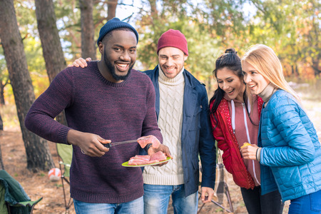 Group of young smiling friends preparing barbecue on a grill in autumn parkの写真素材