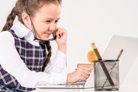 Schoolgirl in glasses sitting at desk with laptopの写真素材