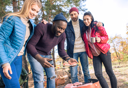 Group of young smiling friends preparing barbecue on a grill in autumn parkの写真素材